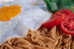 A plate of noodles with an egg and tomato on top