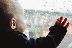 Anonymous baby looking out wet window