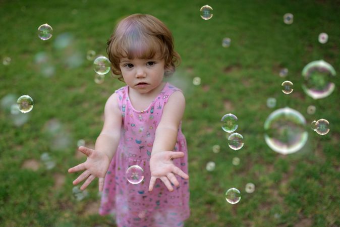 Joyful girl playing with colorful bubbles in grass