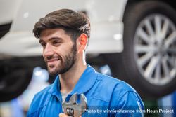 Smiling male mechanic with a beard holding wrench at auto garage 0WeX64