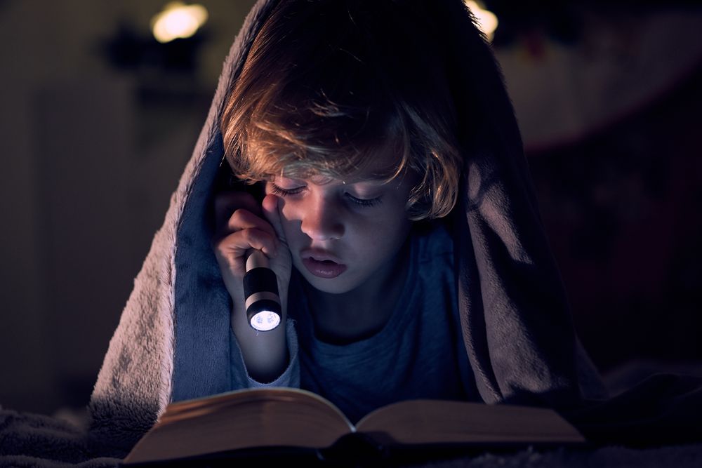 Serious boy reading book in dark apartment