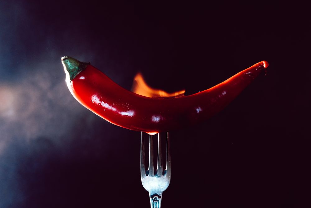 red chili pepper on fire in fork on a dark background