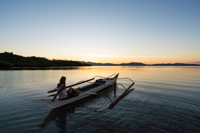 Woman in boat admiring lake at sunset