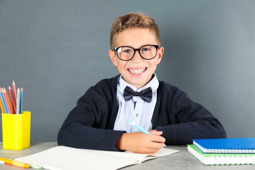 Boy in school uniform sitting at the table against board background
