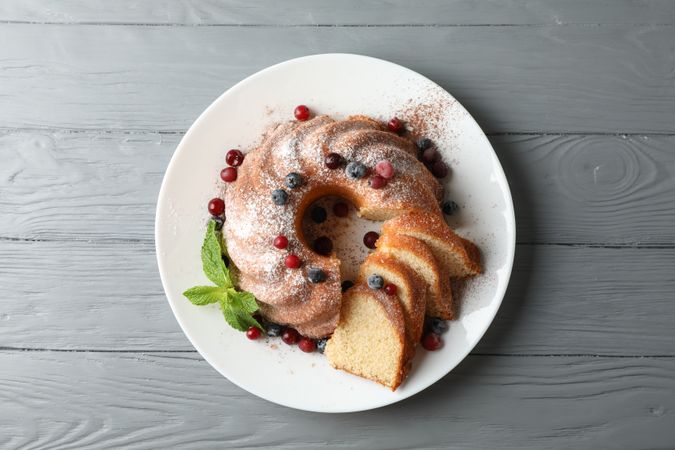 Cake with powdered sugar, berries and mint on wooden background, top view