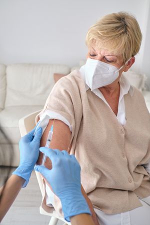 Crop nurse injecting vaccine into arm of elderly patient
