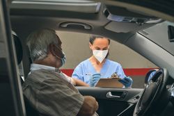 Crop doctor with clipboard against mature patient in car
