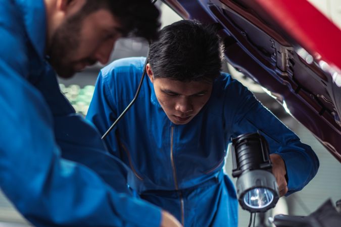 Mechanic shining flashlight to help colleagues repairing car engine at auto garage shop
