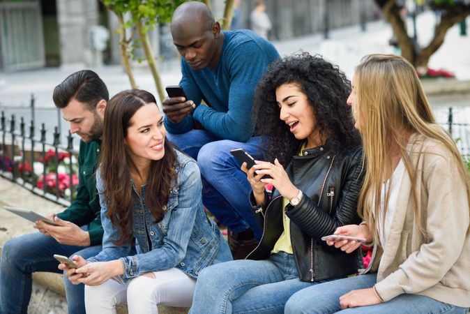 Group of friends hanging out checking phones on ledge outside