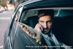 Handsome businessman talking on the mobile phone while sitting on back seat of a car 0JavZb