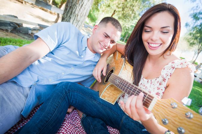 Adult Woman Playing Guitar with Boyfriend In The Park.