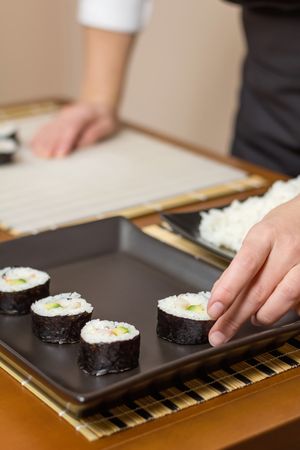 Chef placing Japanese sushi rolls with rice, avocado and shrimps in nori seaweed sheet over a rectangular tray