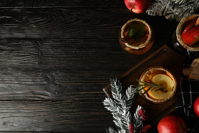 Glasses with apple cider, branches of christmas tree and apples on dark wooden background, space for text