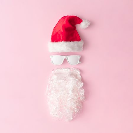 Santa face made of sunglasses, hat and beard on pink background
