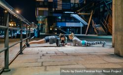Women's sport team doing plank exercises training in city at night 0yXzVa