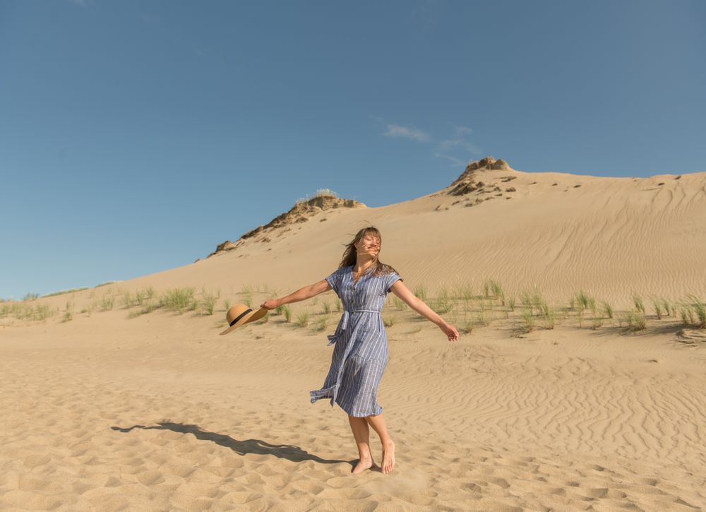 adult woman in casual dress and straw hat running having good time on sand dune