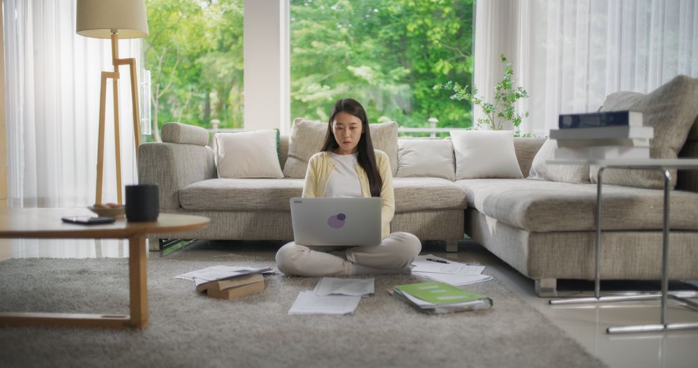 South Korean Woman Sitting on a Floor, Working on Her Project on a Laptop Computer in a Stylish Bright Living Room