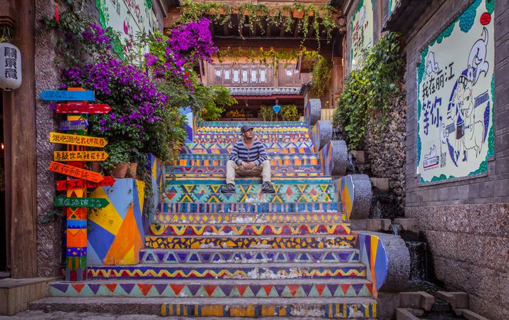 Male tourist sitting on colored stairs in the old city of Lijiang, China