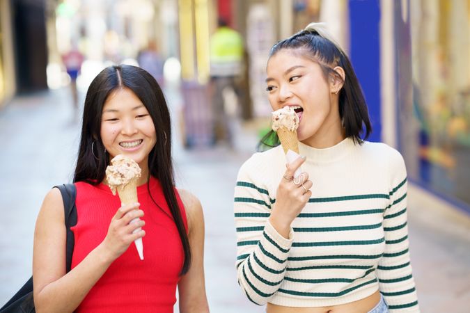 Two women walking down Spanish street enjoying ice cream cones