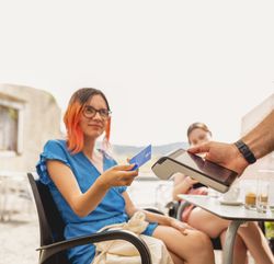 A young person pays with a contactless credit card on a pos payment terminal for the coffees and drinks she had with her friend