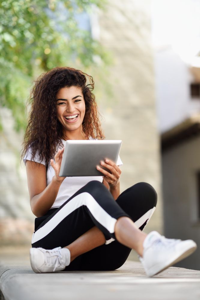 Smiling Arab woman with her digital tablet while sitting outdoors, vertical