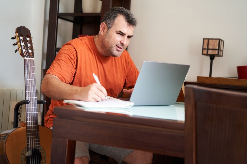 a man with a laptop computer in online guitar lessons writes scales and chords