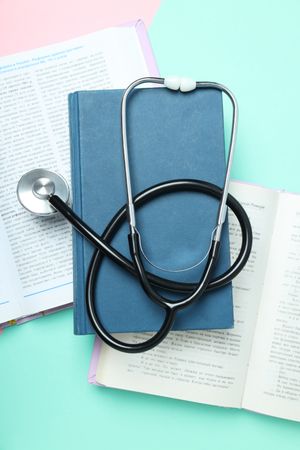 Books and stethoscope on pink and green background, top view