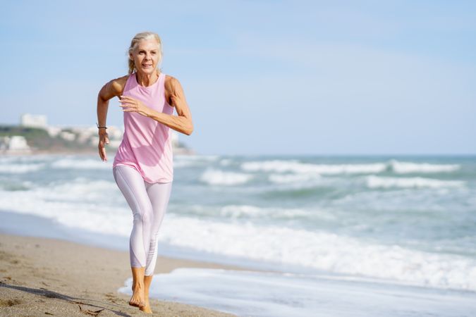 Older female in sports wear jogging along beach