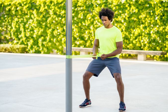 Black male working out with resistant bands wrapped around pole