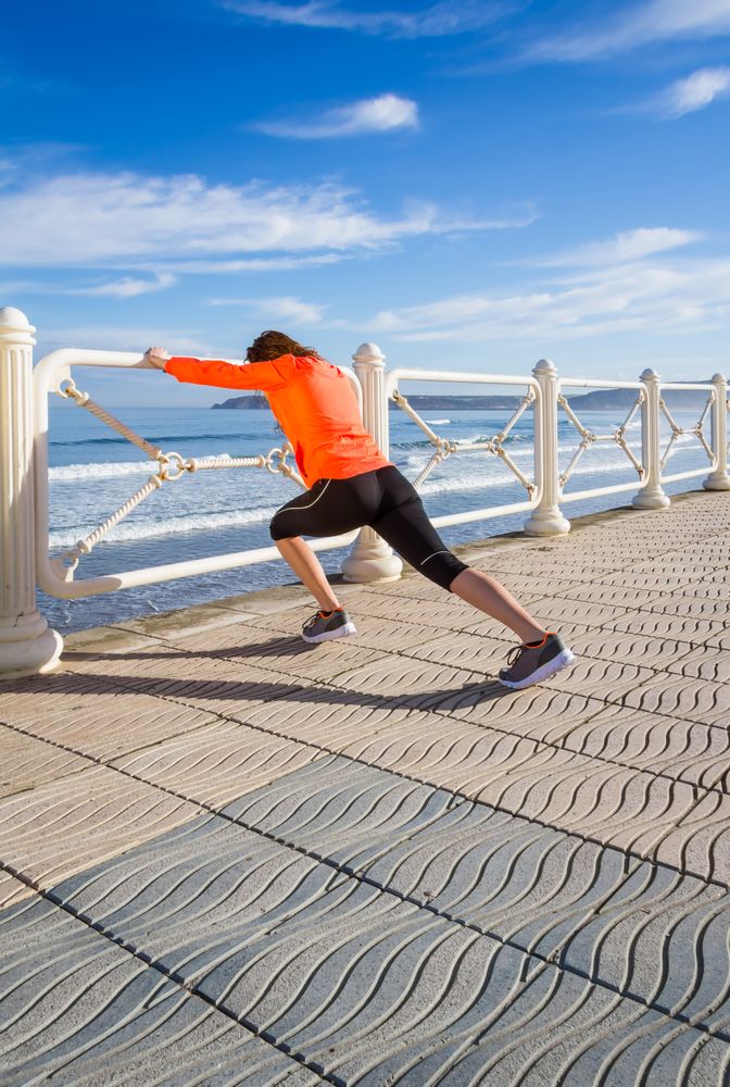Fit woman stretching legs before running on the beach promenade on a summer morning
