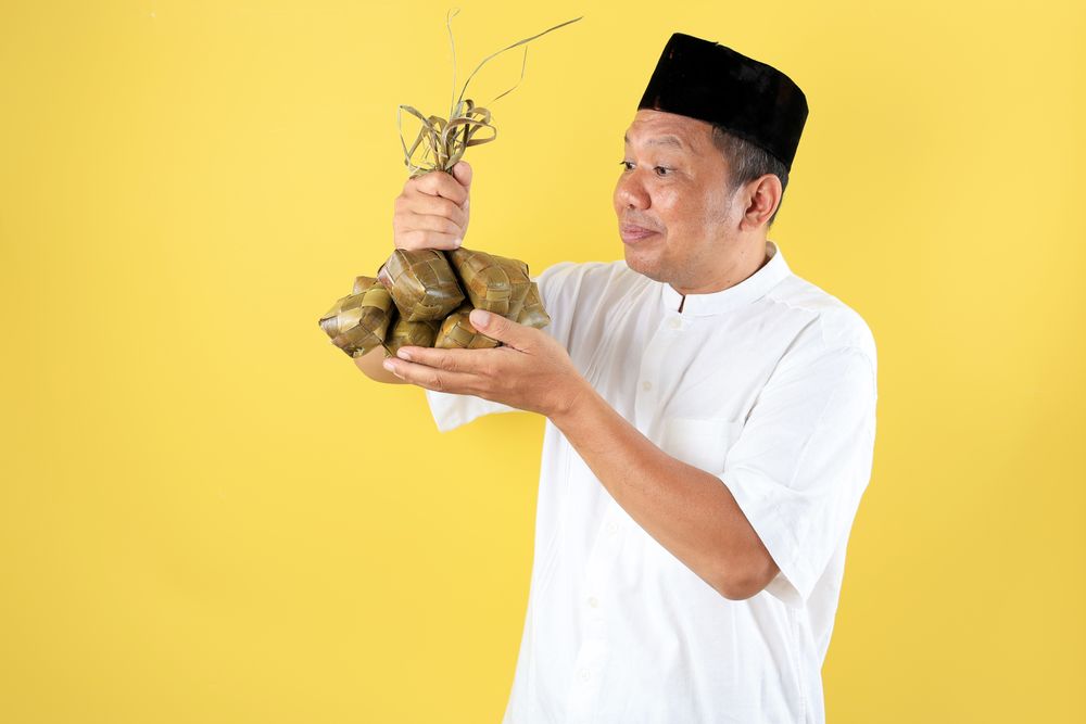 Asian Mature Man Wearing Shirt Baju Koko and Caps Kopyah Holding Ketupat Rice Cakes for Eid al Fitr
