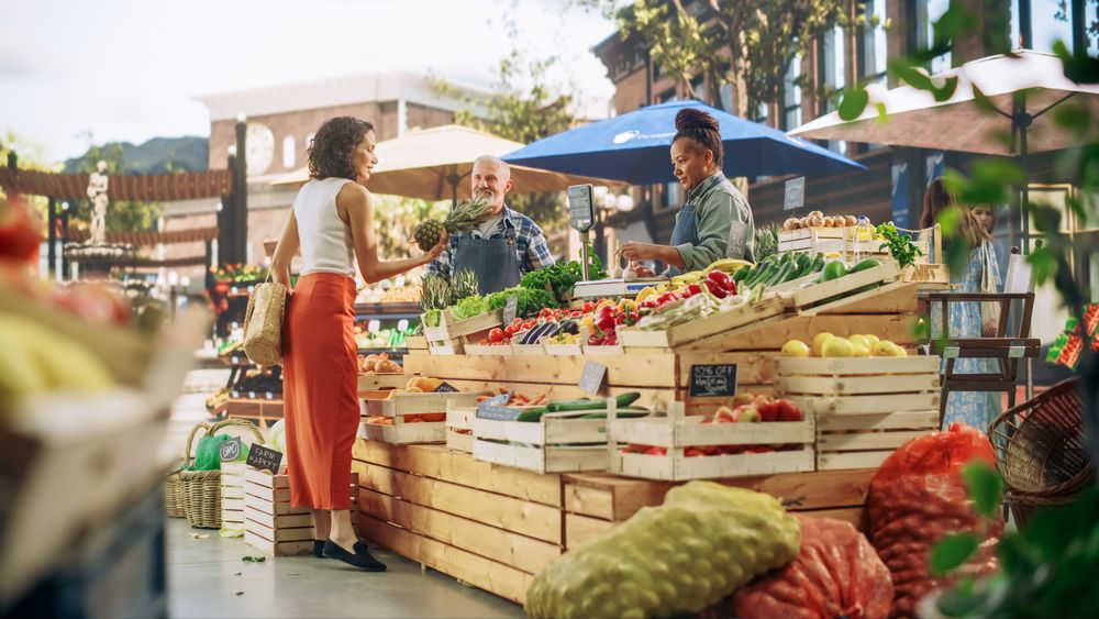 Hispanic Female Customer Buying Two Garlic Heads and a Pineapple From a Multiethnic Farmers Couple.