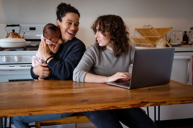 Woman on laptop at kitchen table with partner and baby