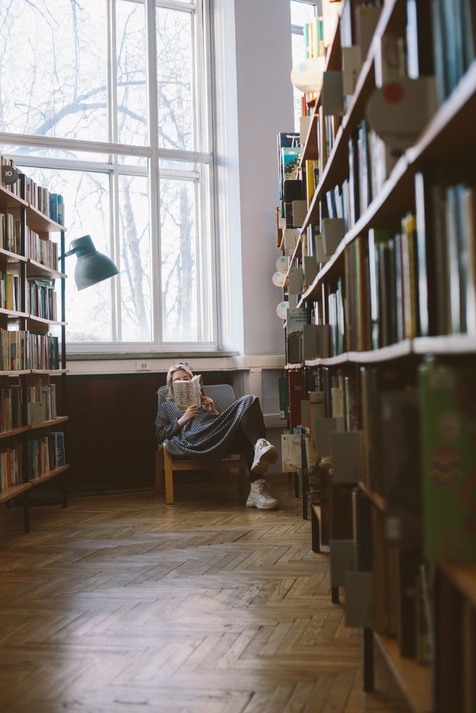 Person sitting on a armchair reading a book in a library