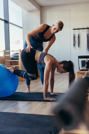 Pilates instructor helping a woman balance her feet on a fitness ball