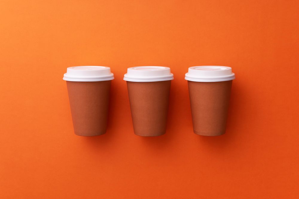 Three disposable coffee cups on orange background