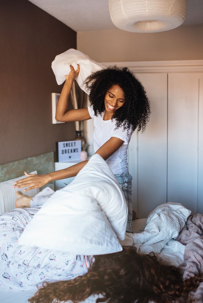 Young female friends fighting with pillows in the bed