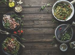 Green pasta on plates, ingredients and kitchen utensils with Parma ham, tomatoes, arugula, cheese and olive oil