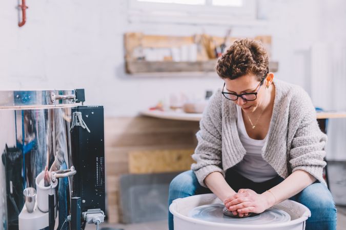 Woman potter shaping vessel on wheel