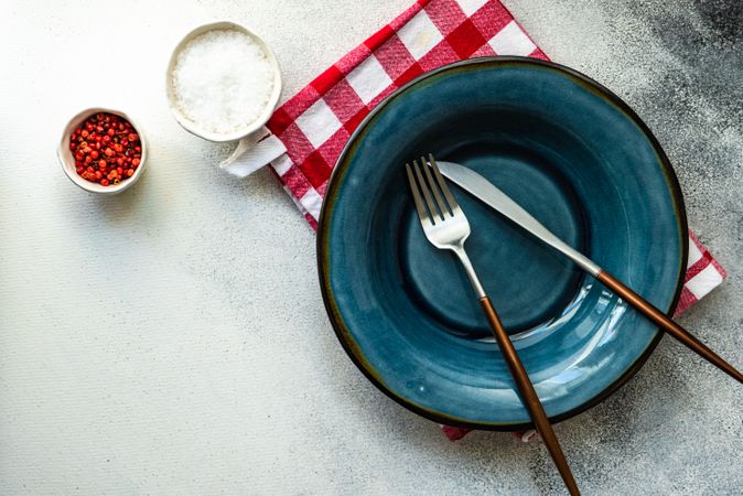 Blue plate on red checkered napkin with salt and peppercorn