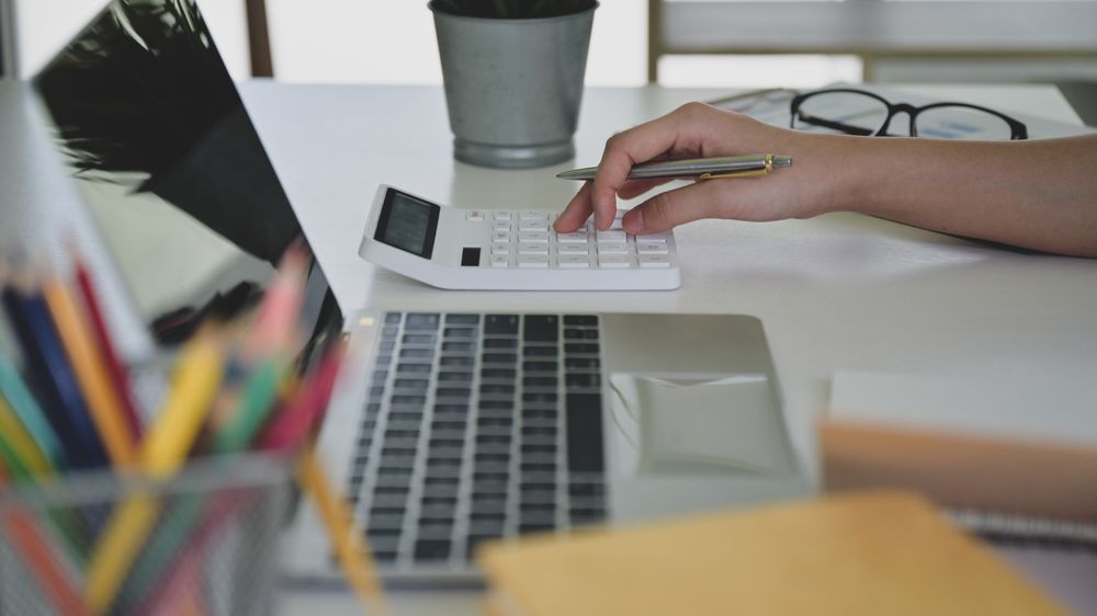Hands using calculator with laptop in front