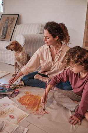 Mother and son painting together in living room near dog