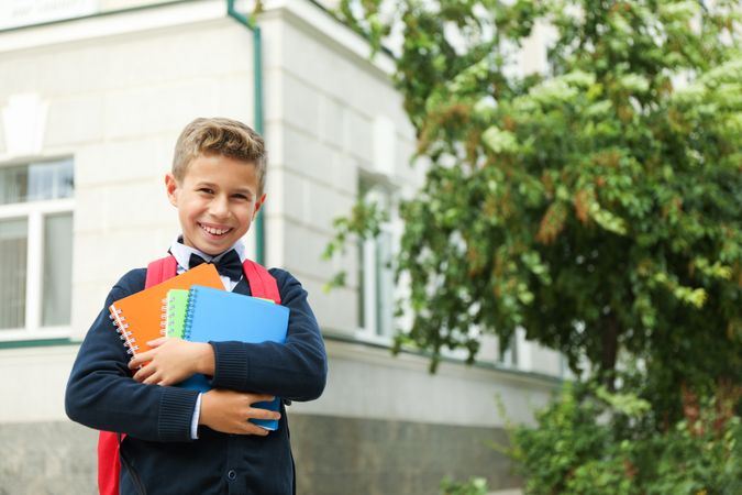 Boy with copybooks against school building, space for text