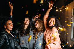 Multi-ethnic group of stylish women celebrating with confetti at night