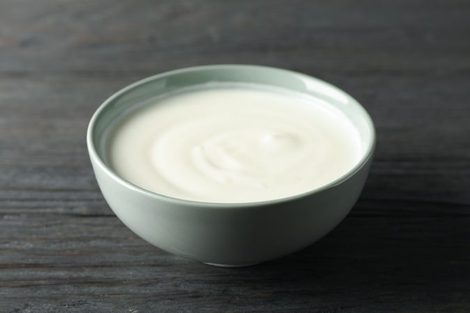 Bowl of sour cream yogurt on dark wooden background