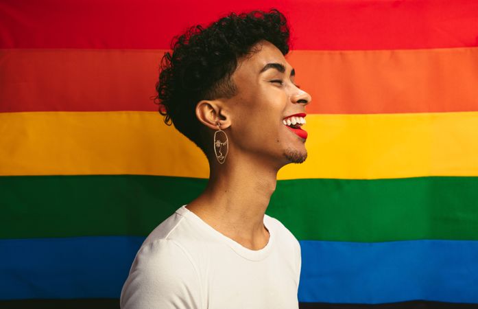 Smiling young man with make up standing against pride flag