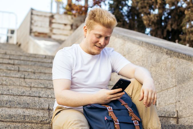 Latino man with albinism using smartphone sitting on city stairs