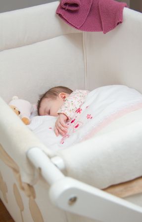 Baby girl sleeping in a cot with pacifier and toy