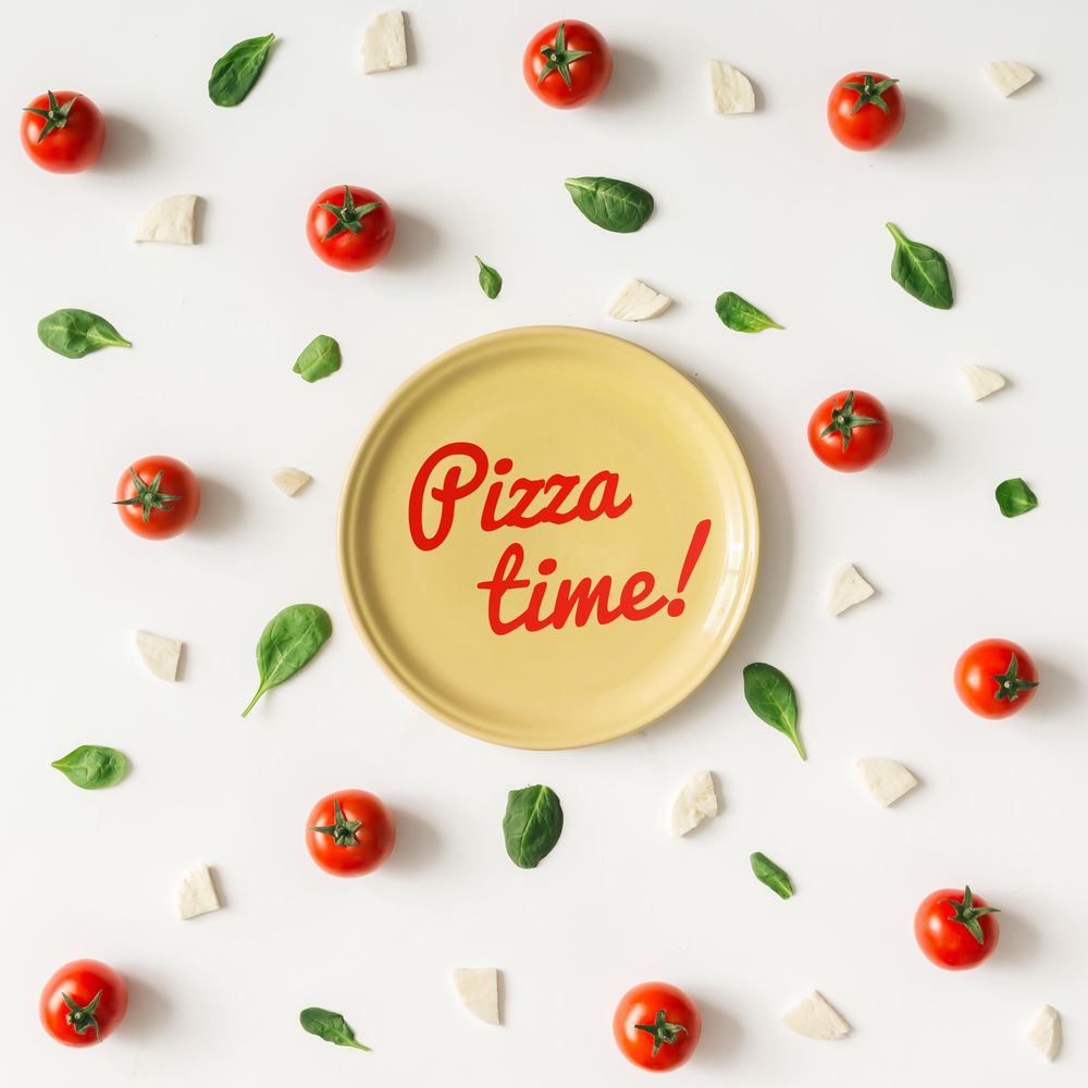 Basil, tomatoes, and cheese on light background with plate and “Pizza time!” text