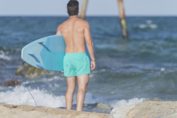 Male surfer with blue board approaching the water